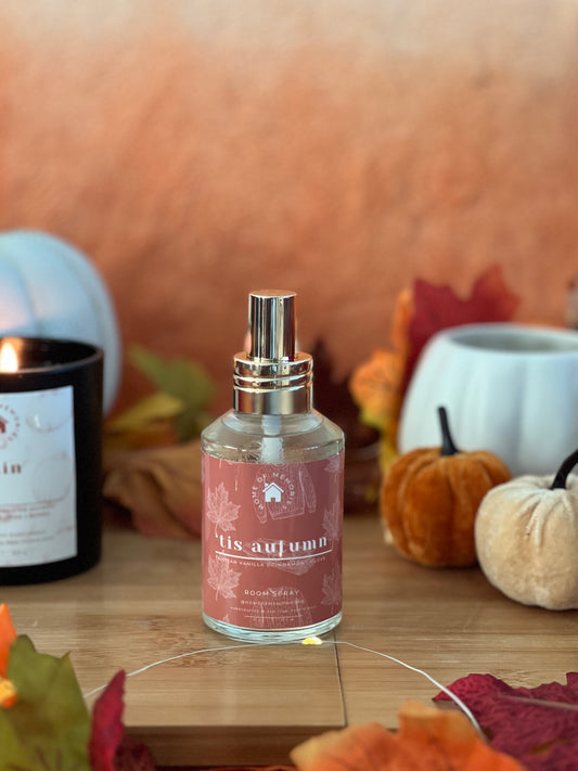 Bottle of 'tis autumn' room spray with fall-themed decor in the background